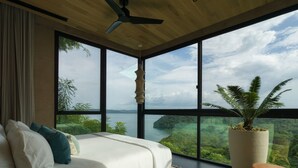 Ein Schlafzimmer mit großem Fenster, einem Bett, einem Deckenventilator und einem Blumentopf.
