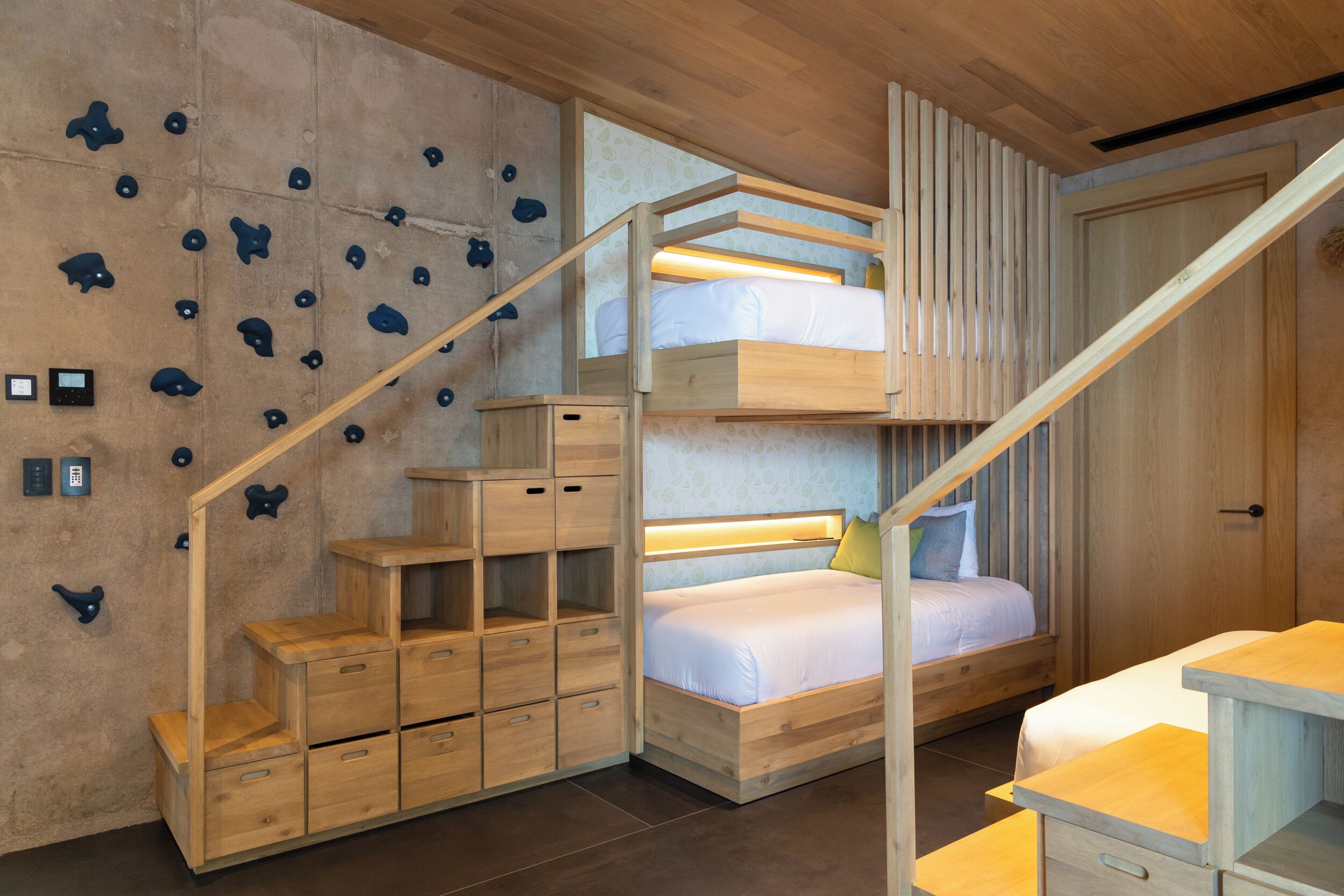 A bunk bed with a wooden ladder, a climbing wall, and built-in storage drawers.