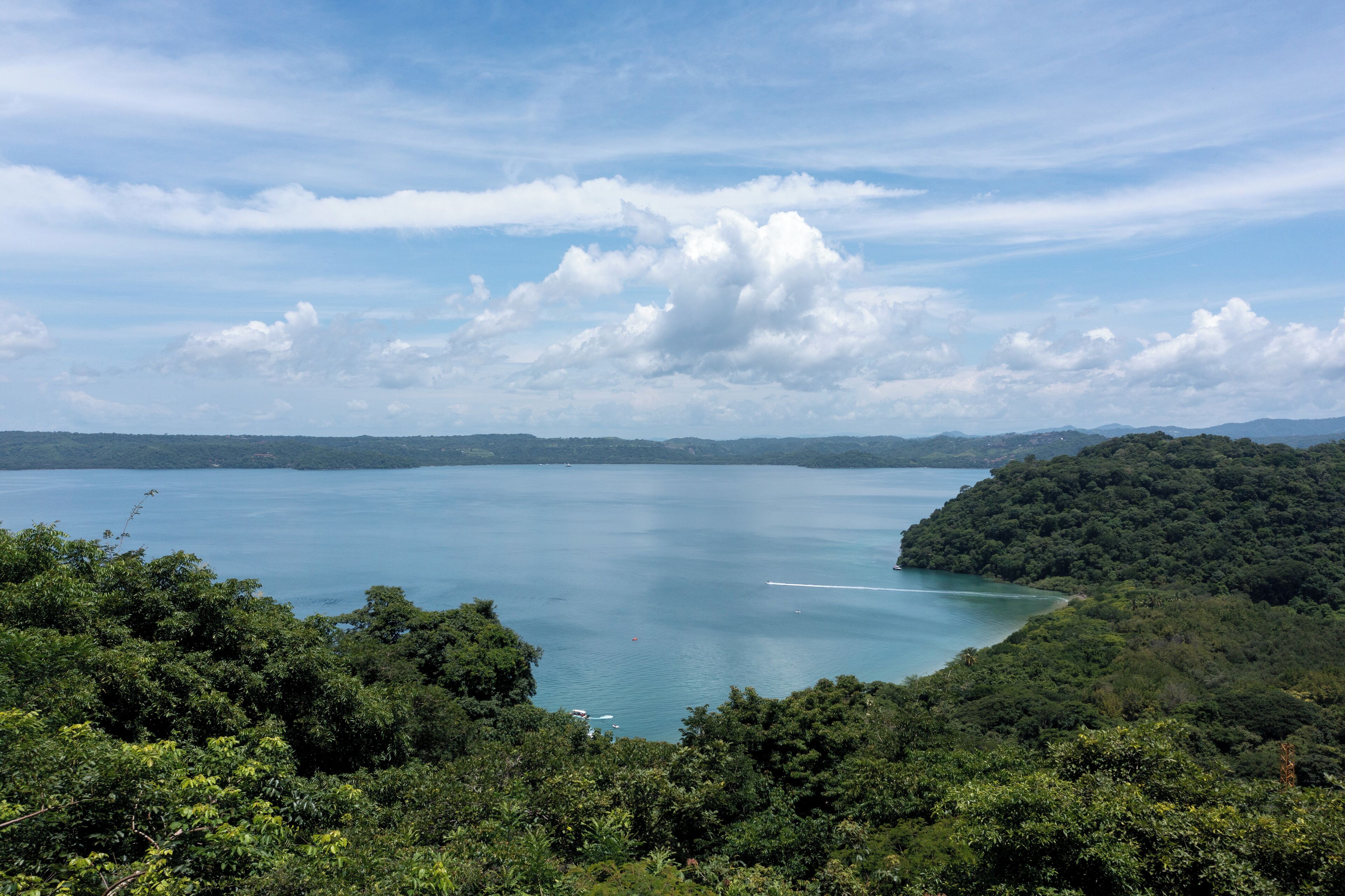 A panoramic view of a lake surrounded by dense forest, with a clear sky above.
