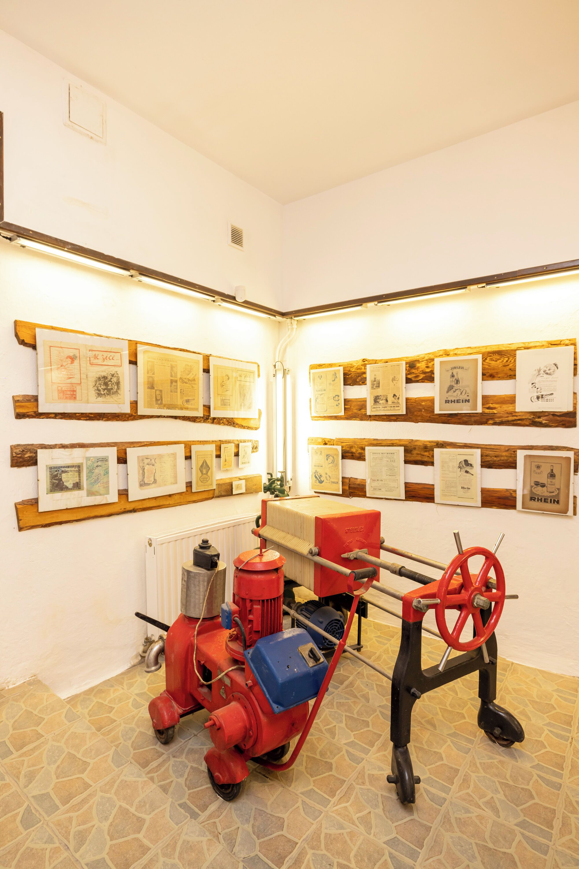 A room with a tiled floor, a red and blue machine, and framed documents on the walls.