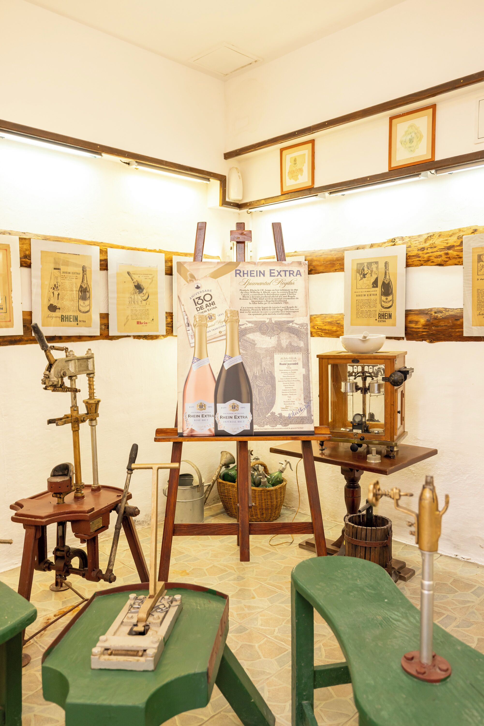 A room with a wooden table, a green chair, a framed poster, and a vintage wine press.