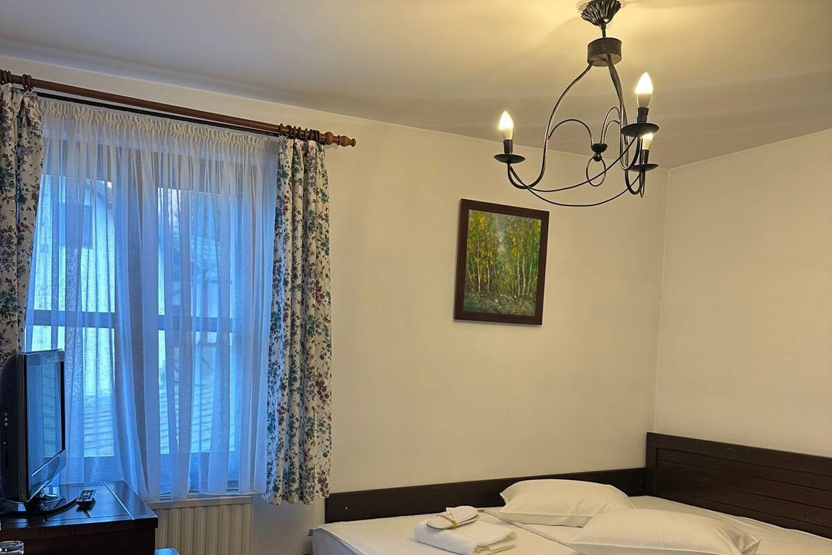A bedroom with a bed, a desk, a chair, a TV, and a painting on the wall.