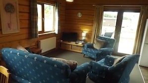 Una habitación estilo cabaña con paredes de madera, un televisor, un sofá y una silla.