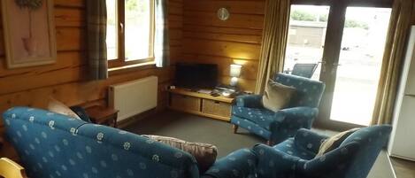 A cabin-style room with wooden walls, a television, a sofa, and a chair.