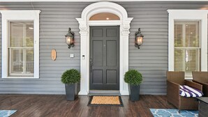 Una casa con fachada gris oscuro, detalles blancos alrededor de la puerta y las ventanas, y dos macetas a cada lado de la entrada.