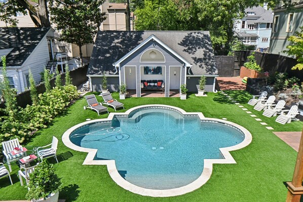 A backyard with a swimming pool, a covered seating area, and lawn chairs.