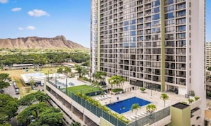 A high-rise hotel with a rooftop pool, multiple floors, and a mountainous backdrop.