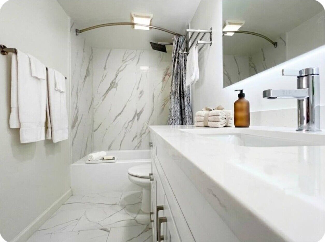 Ein modernes Badezimmer mit Marmorboden, einer Badewanne, einer Toilette, einem Waschbecken mit Spiegel und einer Duschkabine.