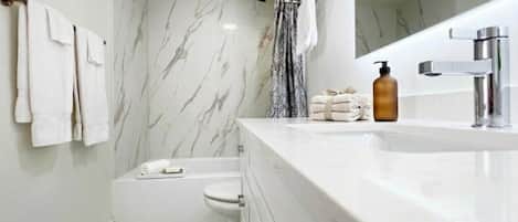 A modern bathroom with a marble floor, a bathtub, a toilet, a sink with a mirror, and a shower area.