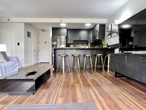 A modern kitchen with dark cabinets, a stainless steel refrigerator, and a bar stool area. - Tropical Oasis, Steps away from Waikiki Beach, Free Parking (Honolulu)