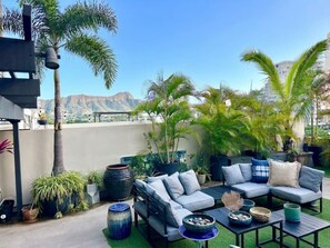 A rooftop patio with a sofa set, planters, and a view of mountains.