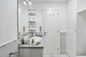 Un baño moderno con un lavamanos blanco, espejo y estanterías con plantas.