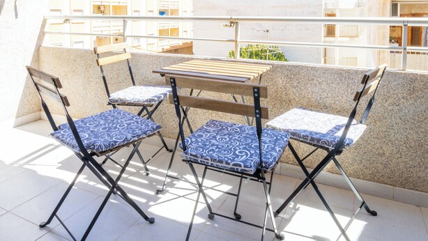 A balcony with a table and four chairs, a striped awning, and a view of buildings in the background. - 2-bedroom Apartment-close to Beaches and Center (Torrevieja)