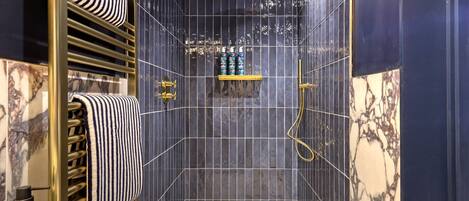 A modern bathroom with a shower, marble tiles, a towel rack, and a shelf with toiletries.