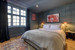 A modern bedroom with a large bed, a window with curtains, a colorful rug, and artwork on the walls. - The Carlton Tavern Hotel (London)