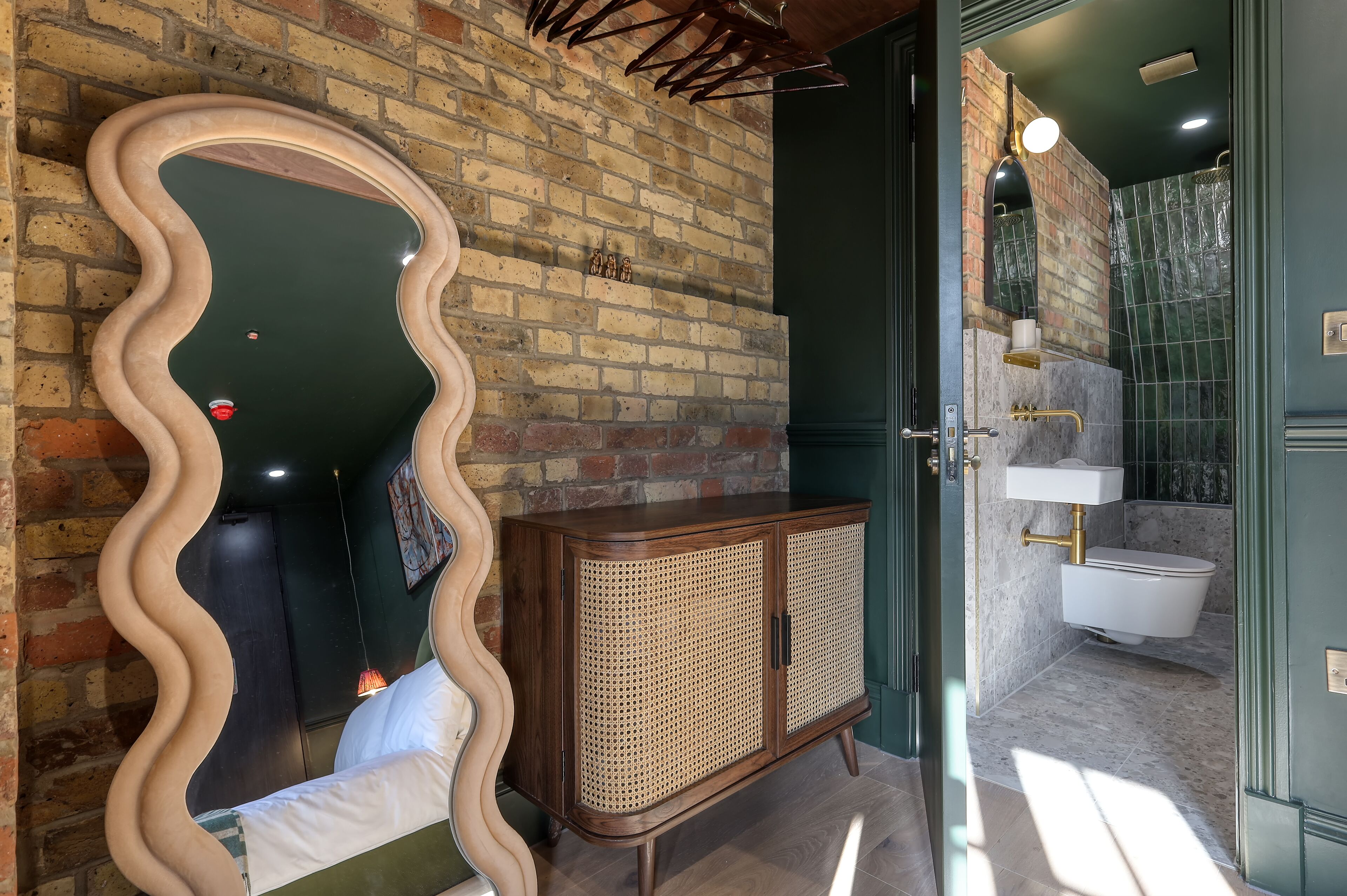 A bathroom with a brick wall, a wooden cabinet, a toilet, and a mirror with a wavy frame.