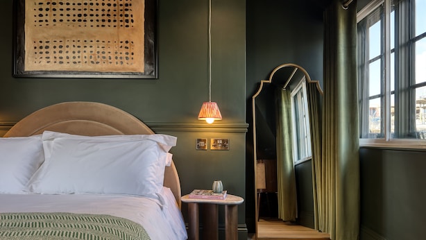 A neatly made bed with white linens, a small table with a book, and a hanging lamp. - The Carlton Tavern Hotel (London)