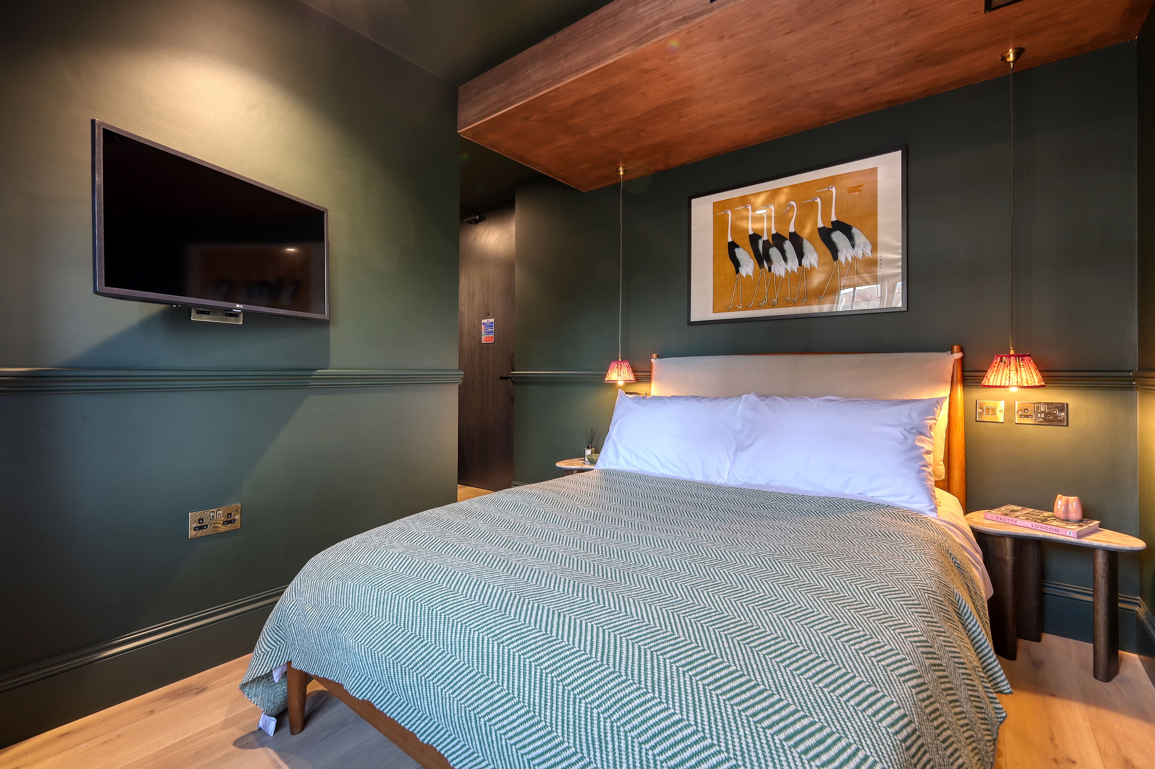 Quarto com cama grande, TV montada na parede, um quadro e luminárias de cabeceira.
