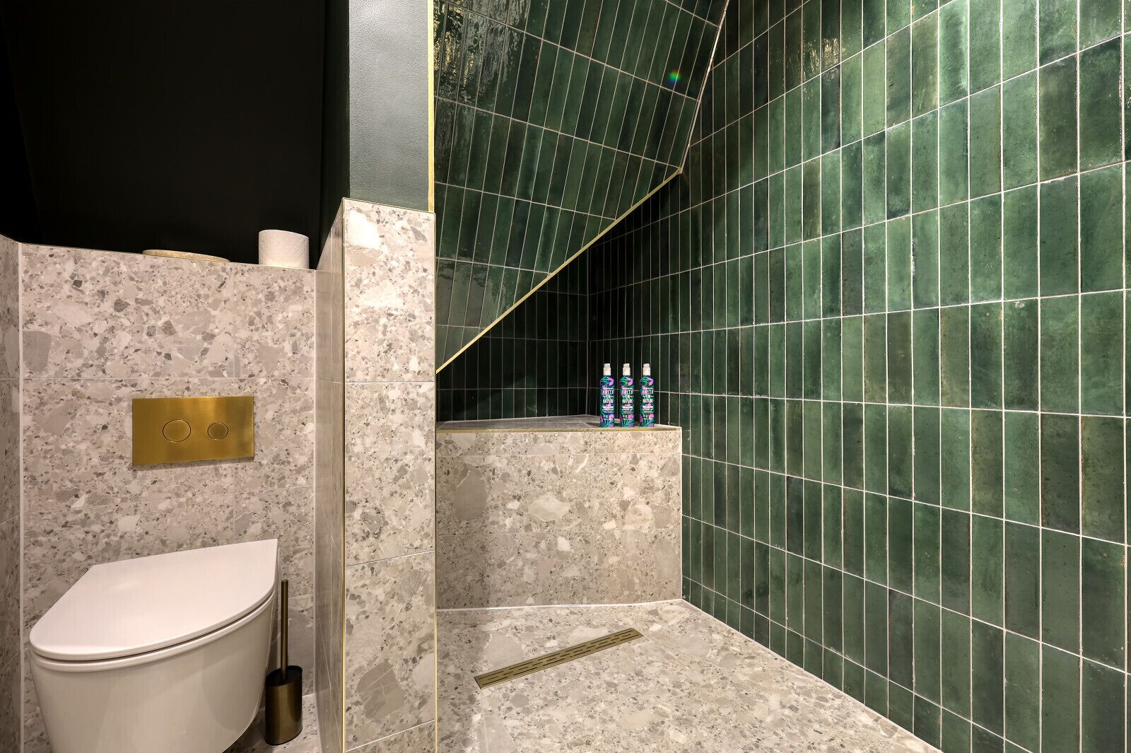 A bathroom with a toilet, a marble sink, and a shower area with green tiles.