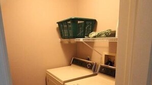 A laundry room with a washing machine, dryer, and shelves above. - King Charles Avenue 408 #2 (Rehoboth Beach)