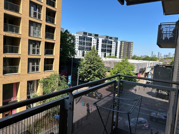 A view from a balcony overlooking a cityscape with modern buildings, a clear sky, and a metal railing. - 1-bed Apt, Sleeps 4, Central To Shops & Transport (London)