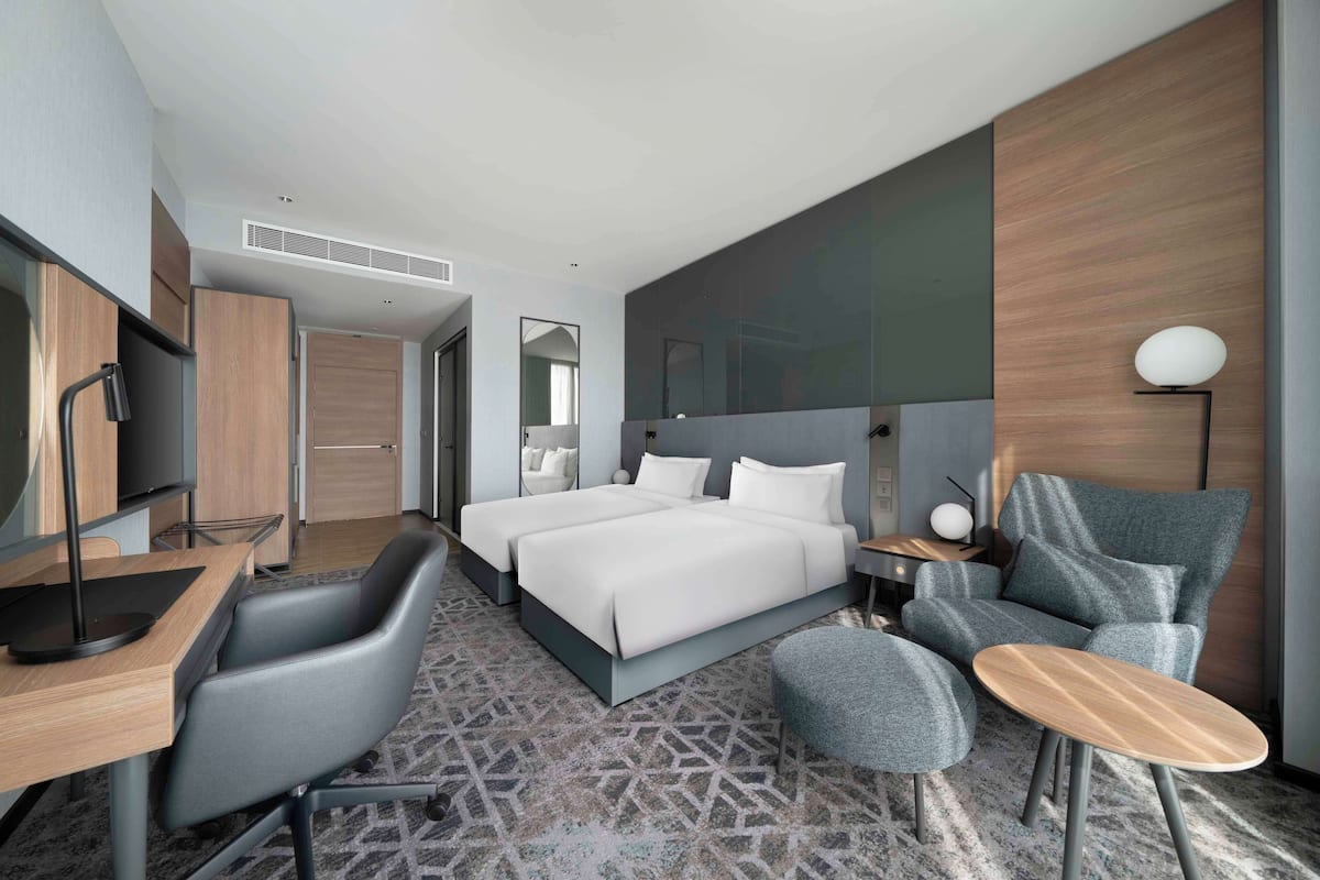 Una habitación de hotel moderna con una cama grande, un escritorio con silla, un sofá y una mesita.