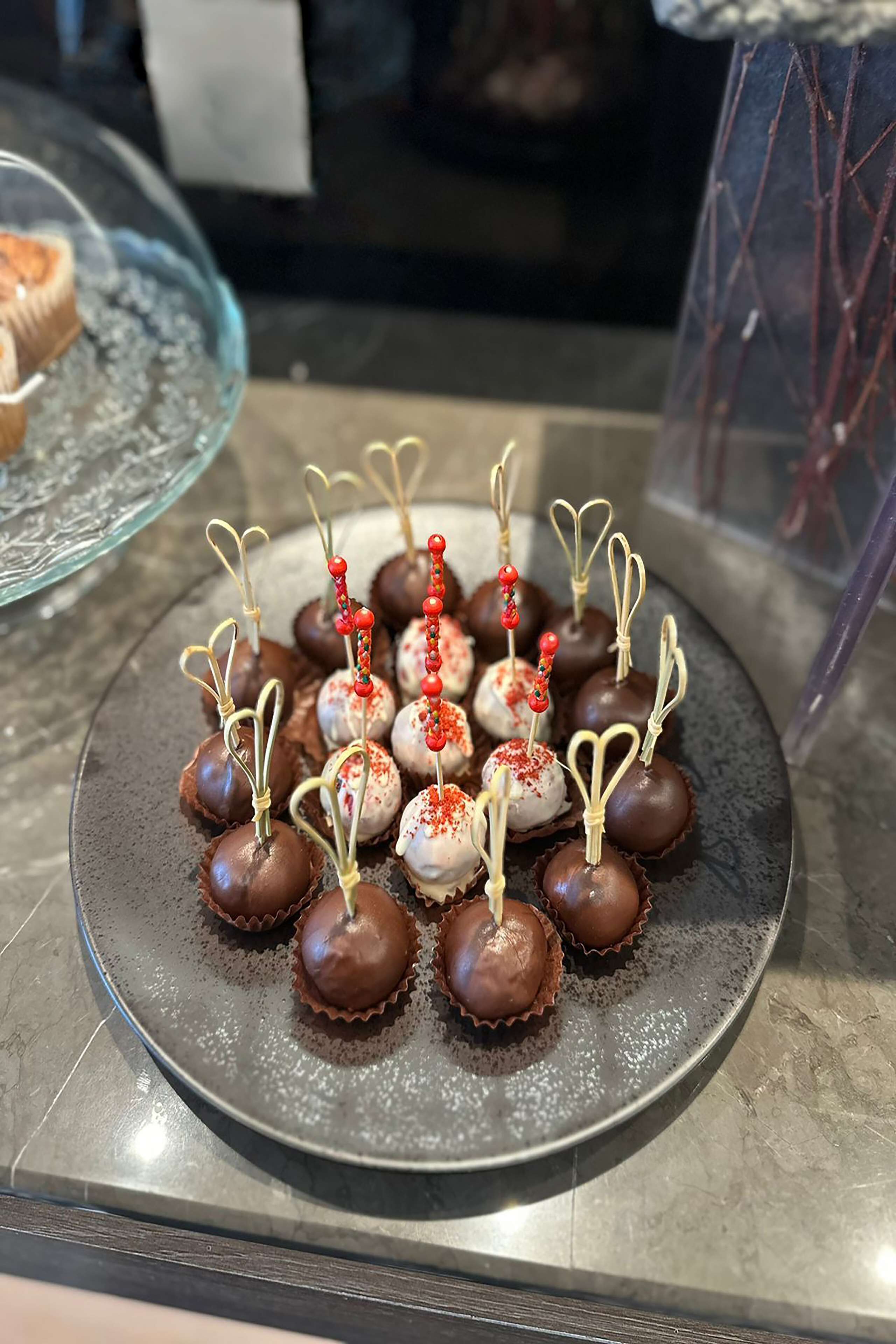 Um prato de doces cobertos de chocolate, com palitos decorativos e granulado vermelho.