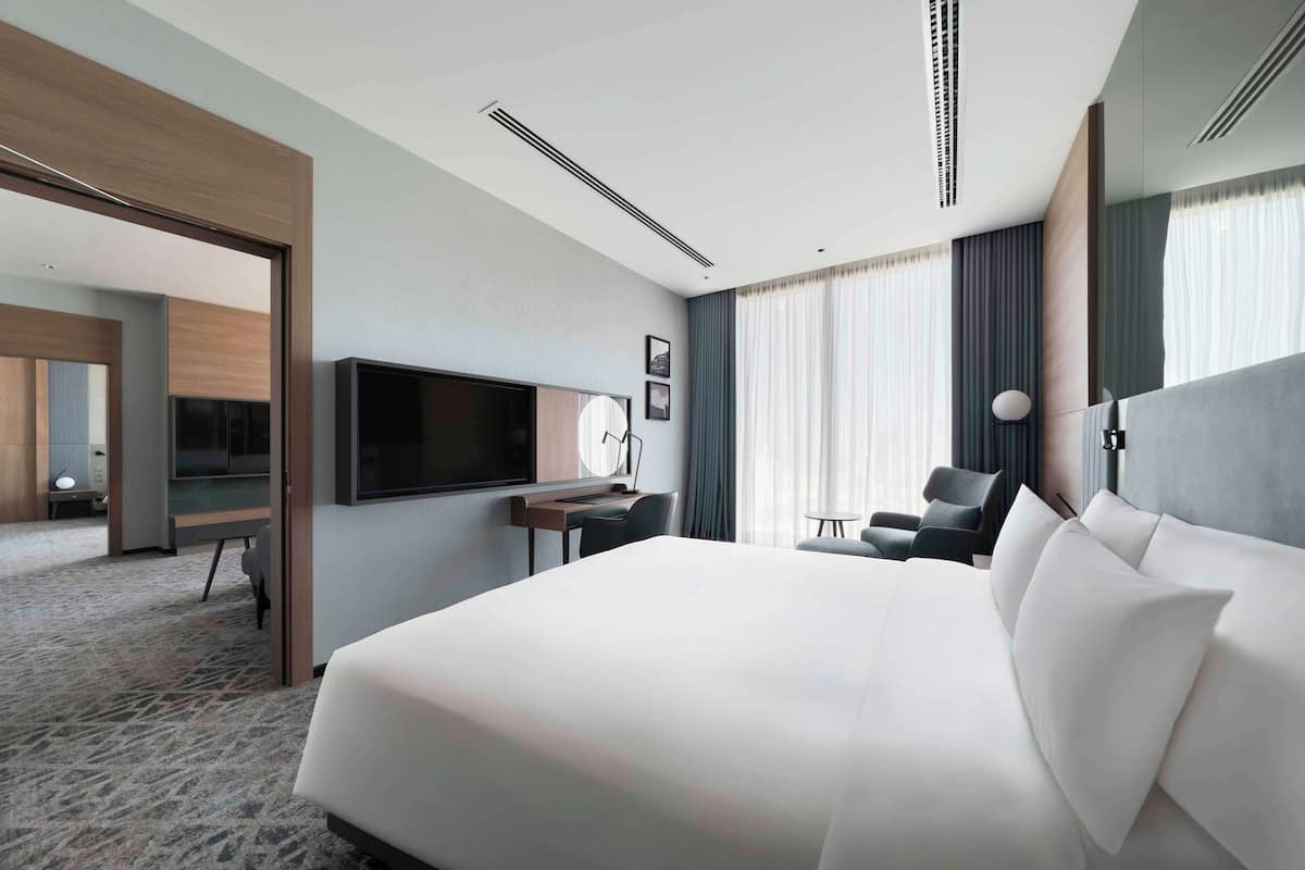 Habitación de hotel moderna con una cama grande, un escritorio, una silla, un televisor y vistas a la ciudad por la ventana.