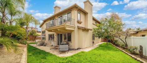 A two-story house with a balcony, a patio with outdoor furniture, and a well-maintained lawn.