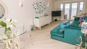 Ein modernes Wohnzimmer mit einem türkisfarbenen Sofa, einem Glastisch und einem Fernseher auf einem Lowboard.
