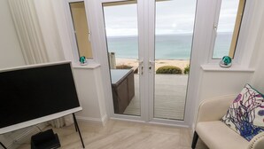 Ein Zimmer mit Fernseher, einer Couch mit einem gemusterten Kissen und Blick auf den Strand durch Glastüren.