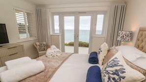 Ein Hotelzimmer mit einem großen Bett, einem Fernseher, Meerblick und einem Balkon.