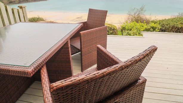 Ein Essplatz aus Rattan auf einer Holzterrasse mit Blick auf Strand und Meer.