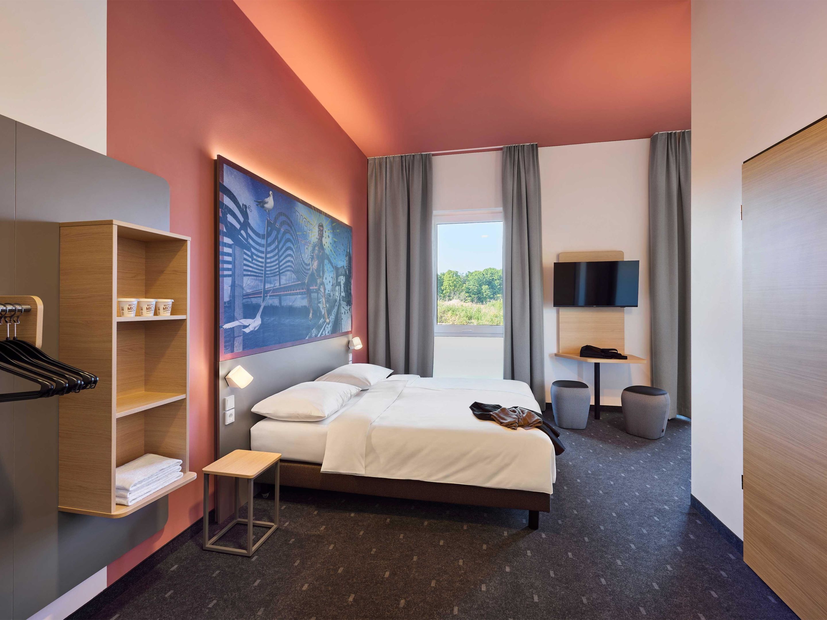 Habitación de hotel moderna con una cama grande, televisión, escritorio y vista a zonas verdes.