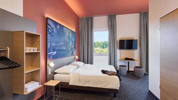 Habitación de hotel moderna con una cama grande, televisión, escritorio y vista a zonas verdes.