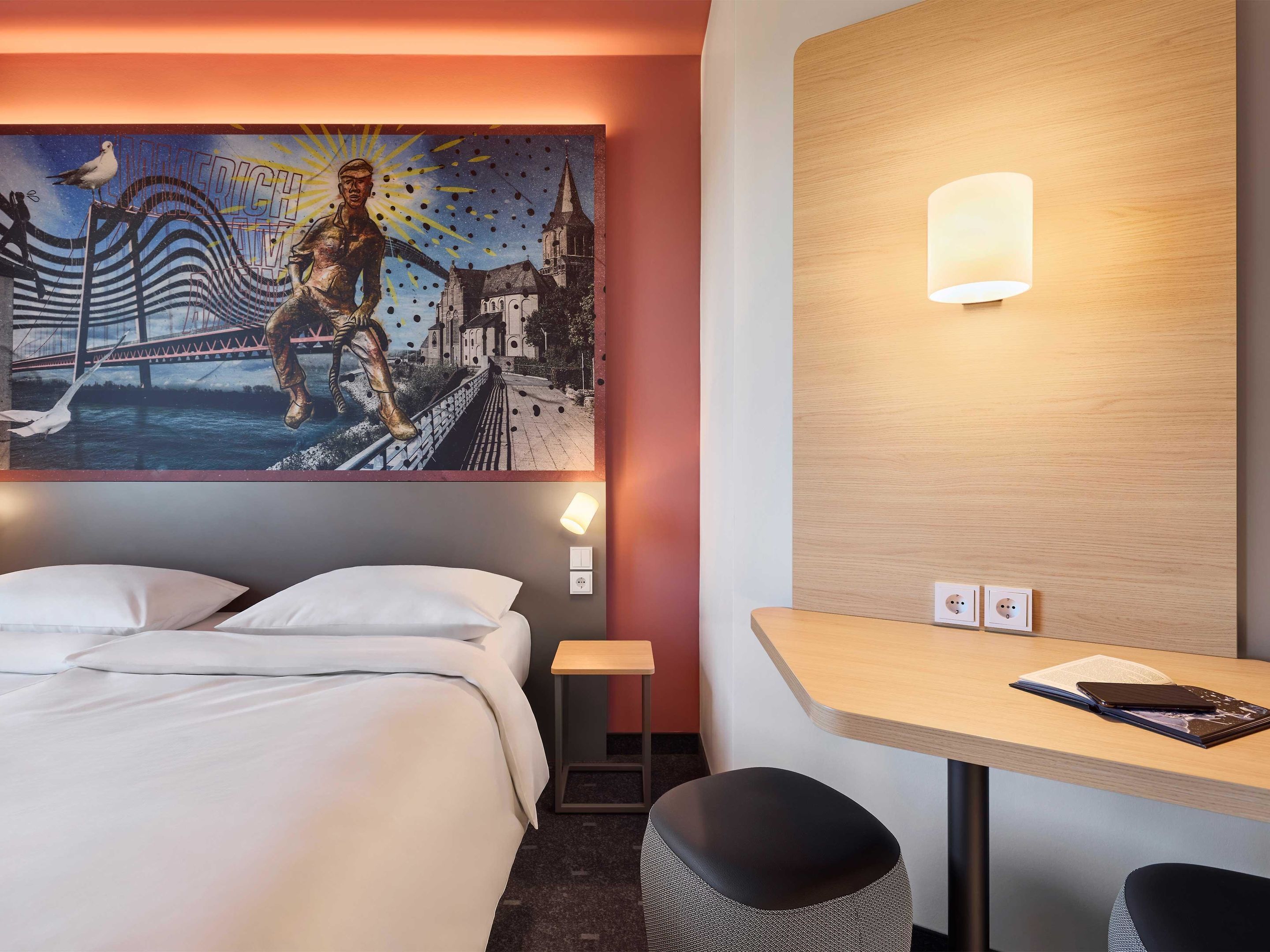 Une chambre d’hôtel avec un lit, un bureau et une lampe fixée au mur.