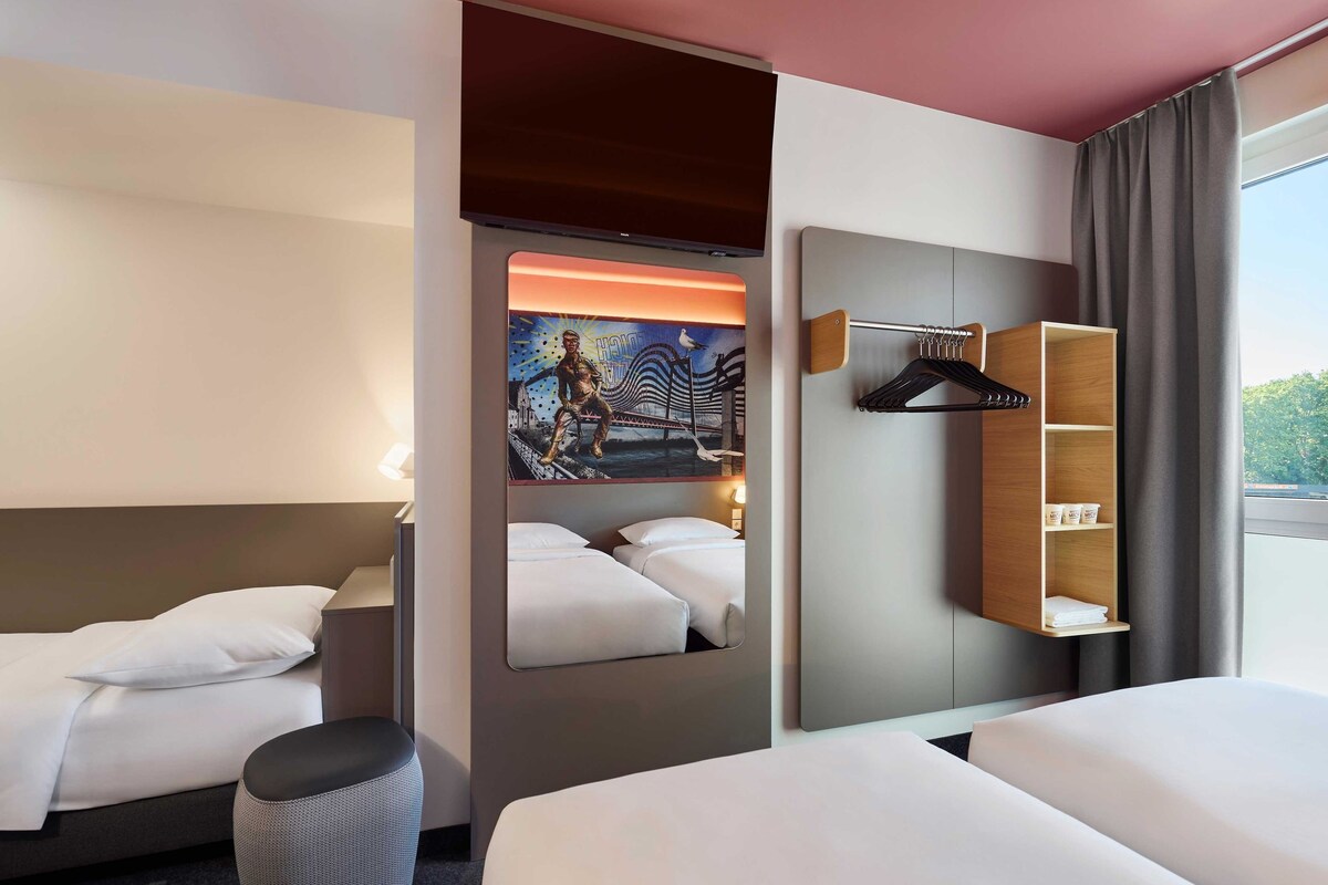 Een hotelkamer met twee bedden, een grote spiegel, een schilderij en een houten plankje met toiletartikelen.