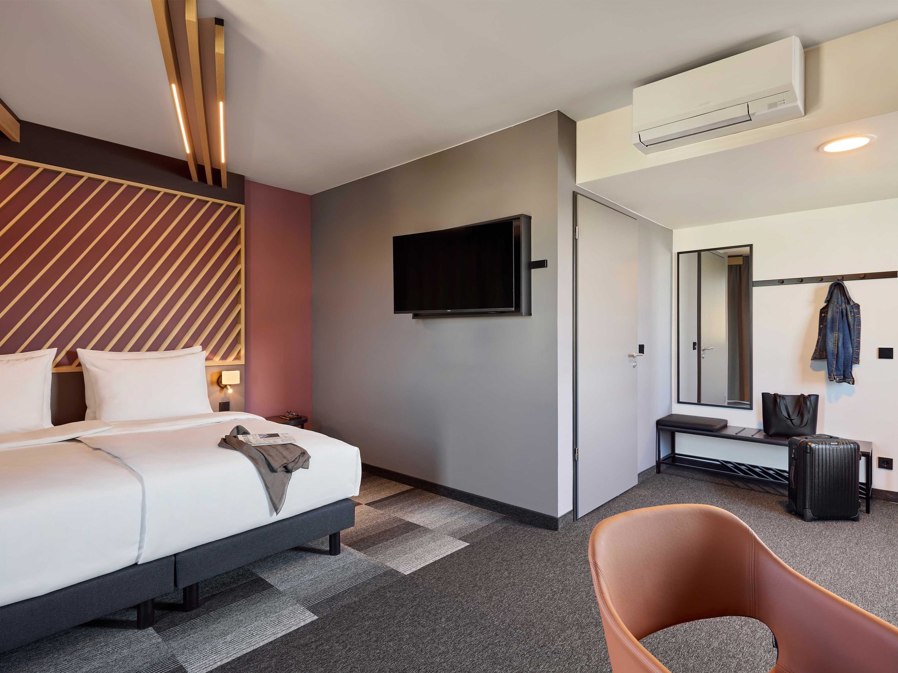 Une chambre d’hôtel moderne équipée d’un lit, d’une table de chevet, d’une télévision et d’un coin salon avec une chaise et un banc.
