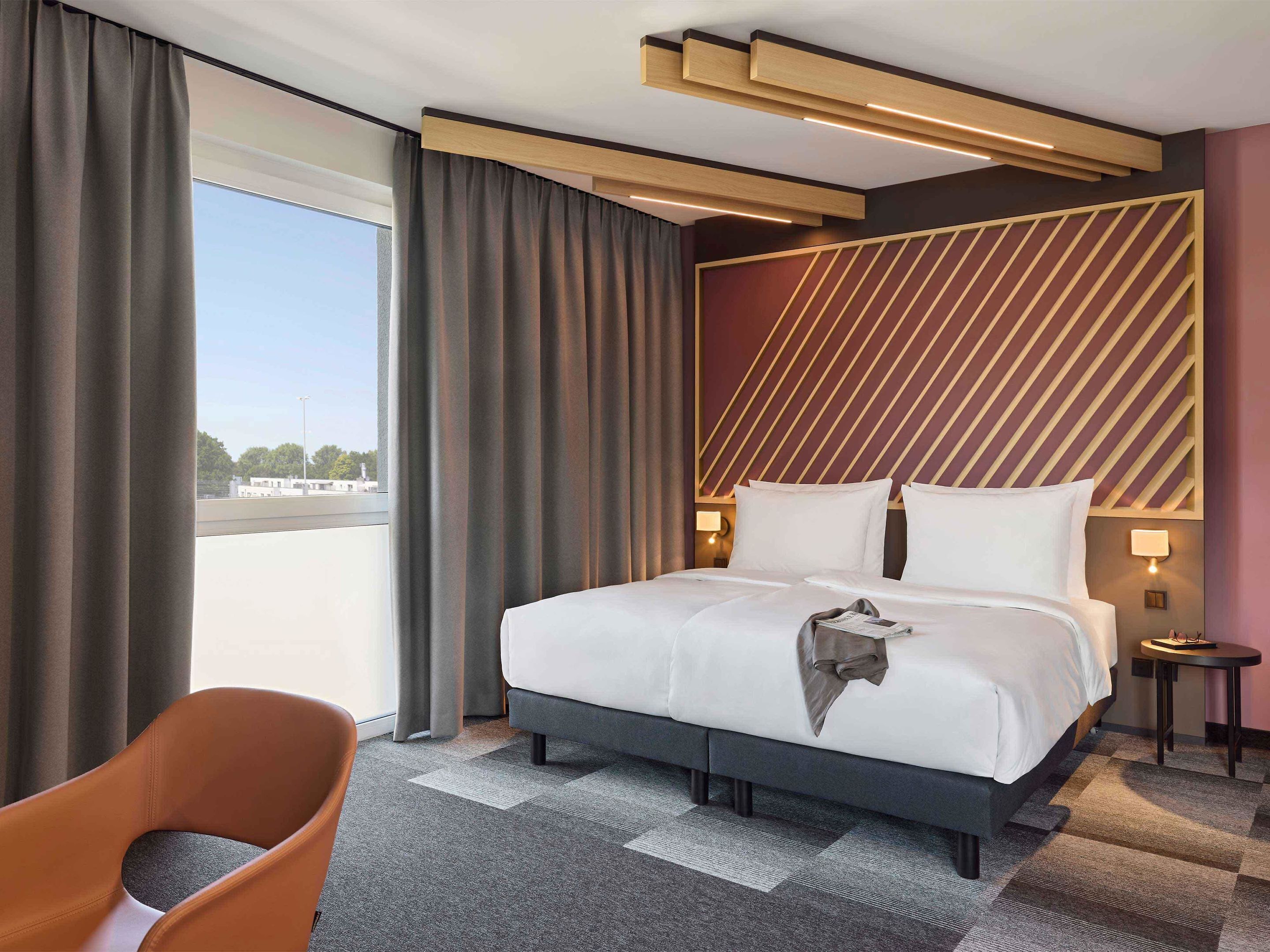 Una habitación de hotel moderna con una cama grande, vistas a la ciudad y una mesita auxiliar.