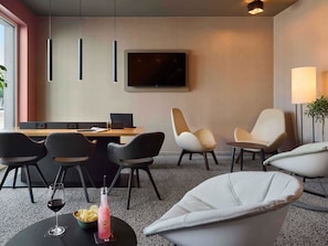 A modern hotel room with a desk, two chairs, a sofa, a TV, and a plant. - B&B HOTEL Emmerich (Emmerich)