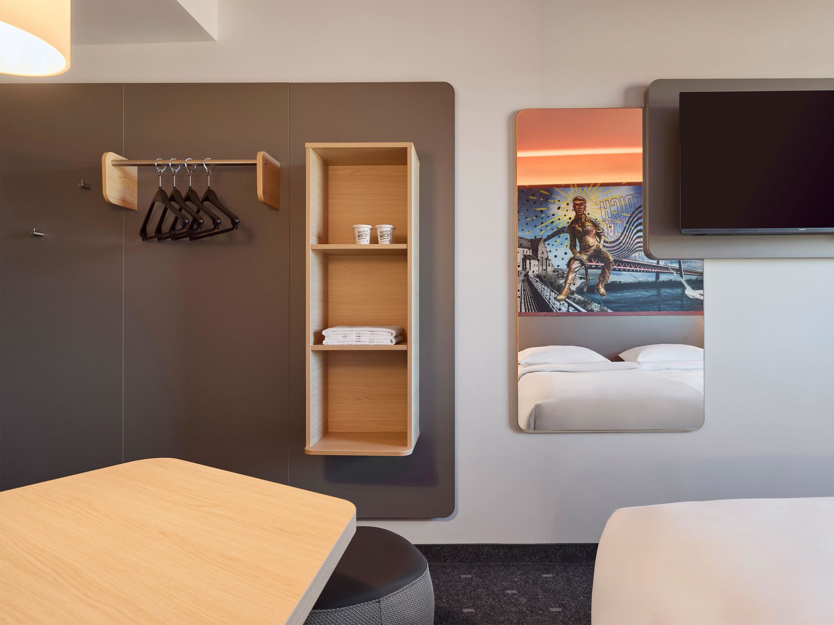 Habitación de hotel con una estantería de madera, un televisor de pantalla plana y un cuadro de un atardecer.