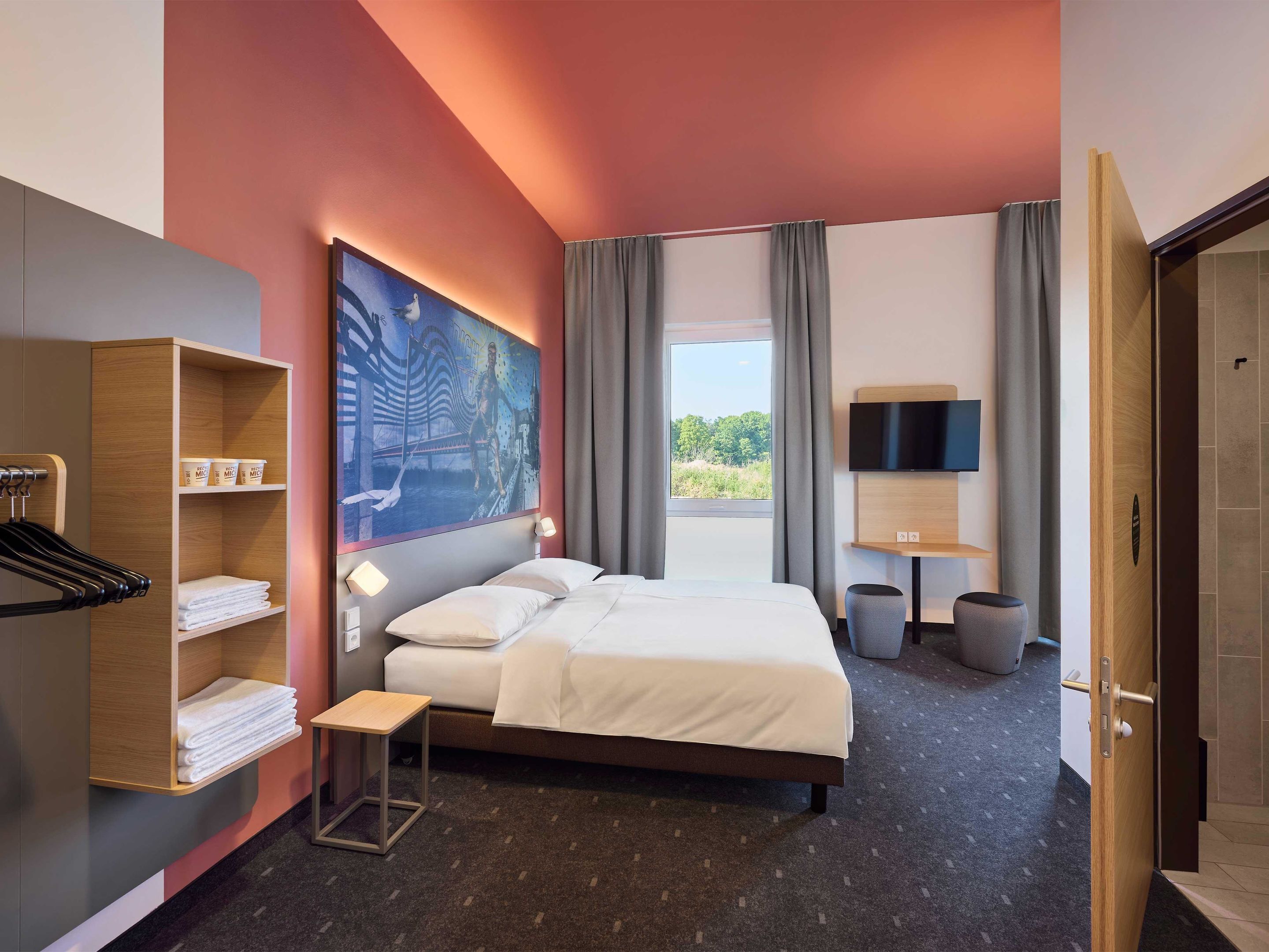 Una habitación de hotel con cama, televisión, un cuadro y vista a áreas verdes.