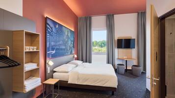Una habitación de hotel con cama, televisión, un cuadro y vista a áreas verdes.