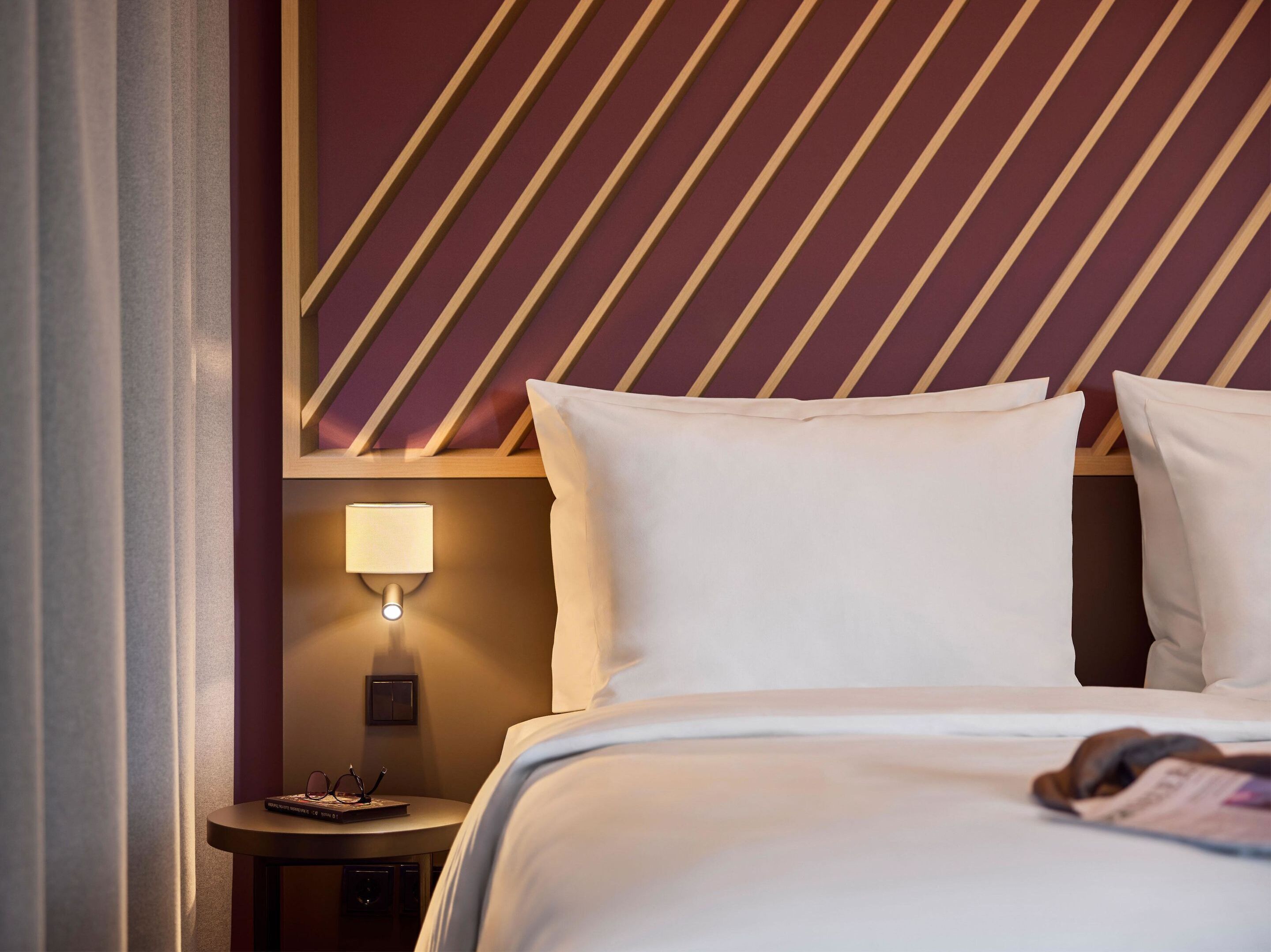 A hotel room with a bed, a nightstand with a lamp, and a wall with a striped pattern.