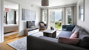 Una sala moderna con sofá, una mesa de centro, televisor y una silla. Hay una puerta corrediza de vidrio que da a un balcón con vistas.