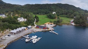 Vista aérea de una zona costera con un puerto deportivo, casas y una colina boscosa.