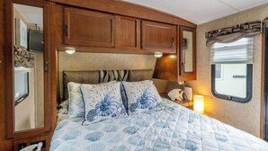 Quarto com cama, armários de madeira, janela e espelho.