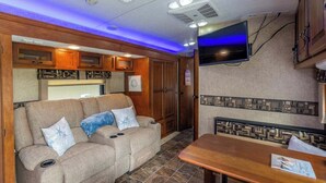 Interior acolhedor de uma RV com sofá, mesa de jantar e televisão montada.