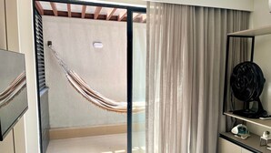 Een slaapkamer met een bed, nachtkastje, spiegel, ventilator en hangstoel.