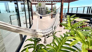Een overdekte buitenruimte met een hangmat, tafels, stoelen en plantenbakken.